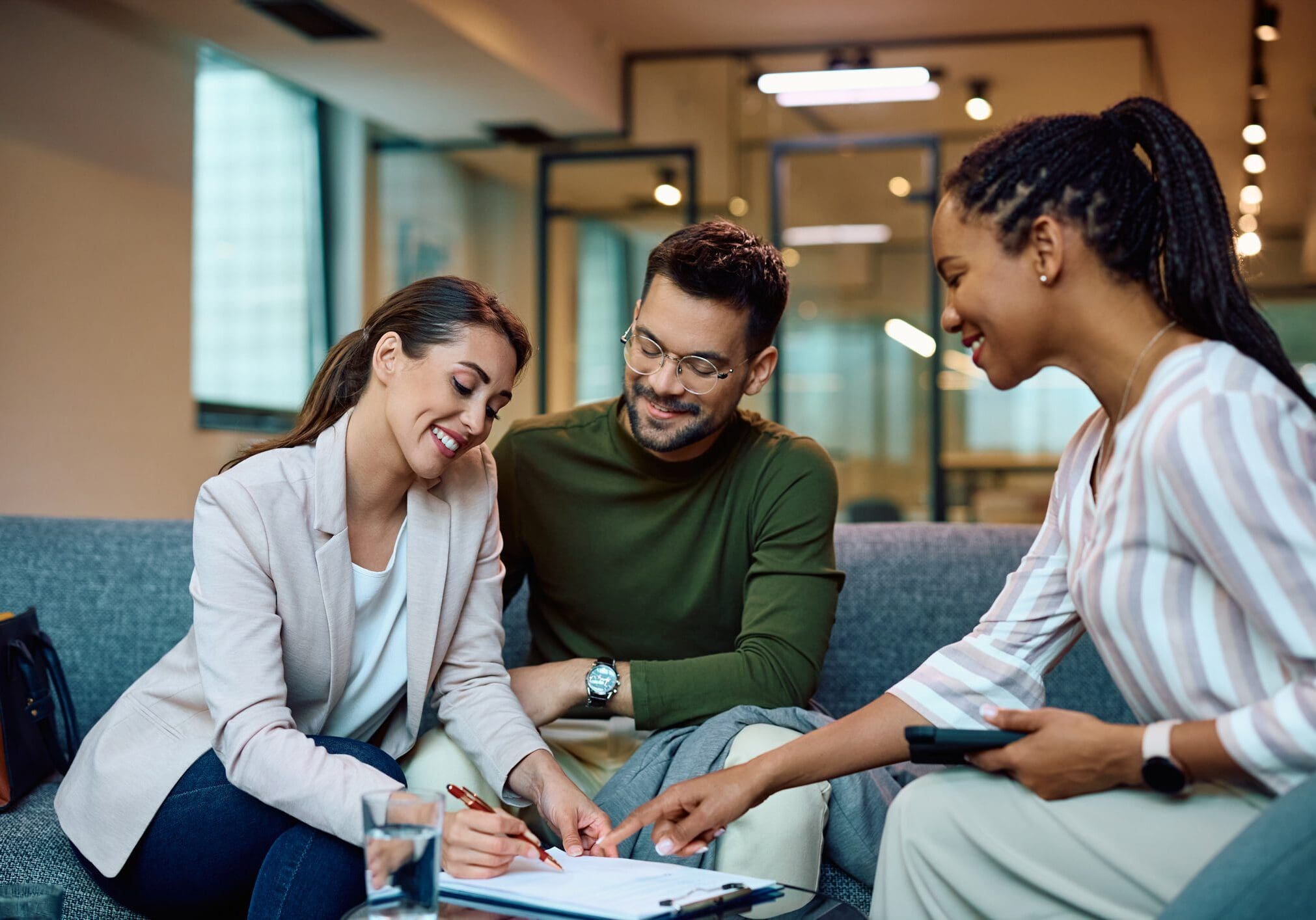 Three people discussing paperwork on couch.