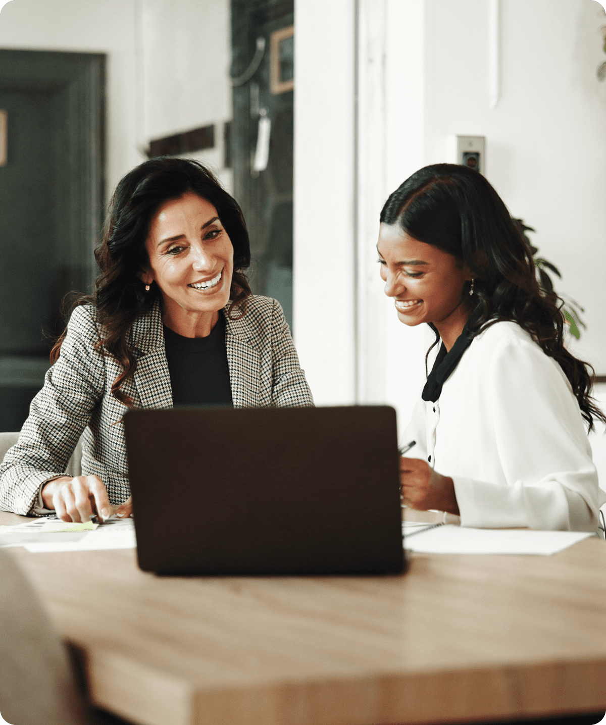 Two women smiling while working on laptop.